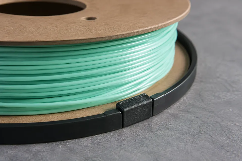 A black protective ring and clip seated on a cardboard filament spool flange.