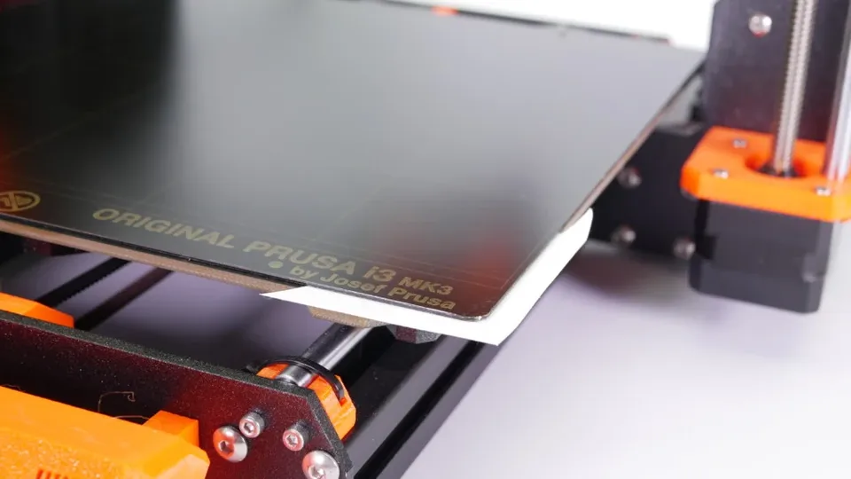 An incorrectly seated removable steel print sheet resting above the edge of a Prusa printer bed.